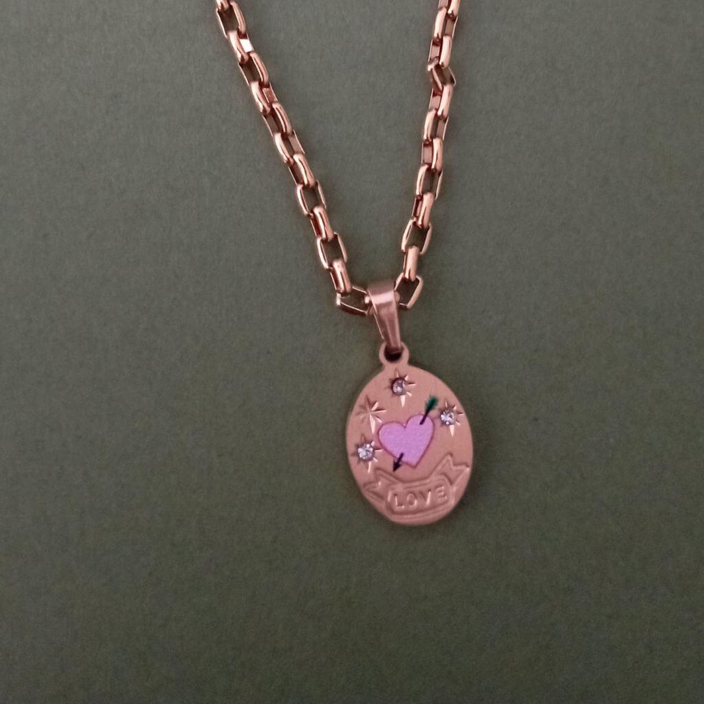 Este collar Corazón Rose Gold es una pieza elegante y sofisticada. Cuenta con un colgante en forma de medalla grabado con un corazón rosa y una flecha, adornado con pequeños brillantes. Con este collar, podrás lucir un look único y femenino.