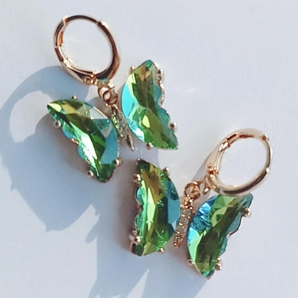 Estos elegantes pendientes en forma de mariposa cuentan con cristales verdes colgando de un mini aro. Con un toque de color y un diseño único, son perfectos para cualquier ocasión. Disfruta de su belleza y añade un toque de sofisticación a tu estilo.