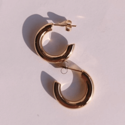 Imagen de pendientes de aro forma C gruesos en fondo rosa con sombra de sol
